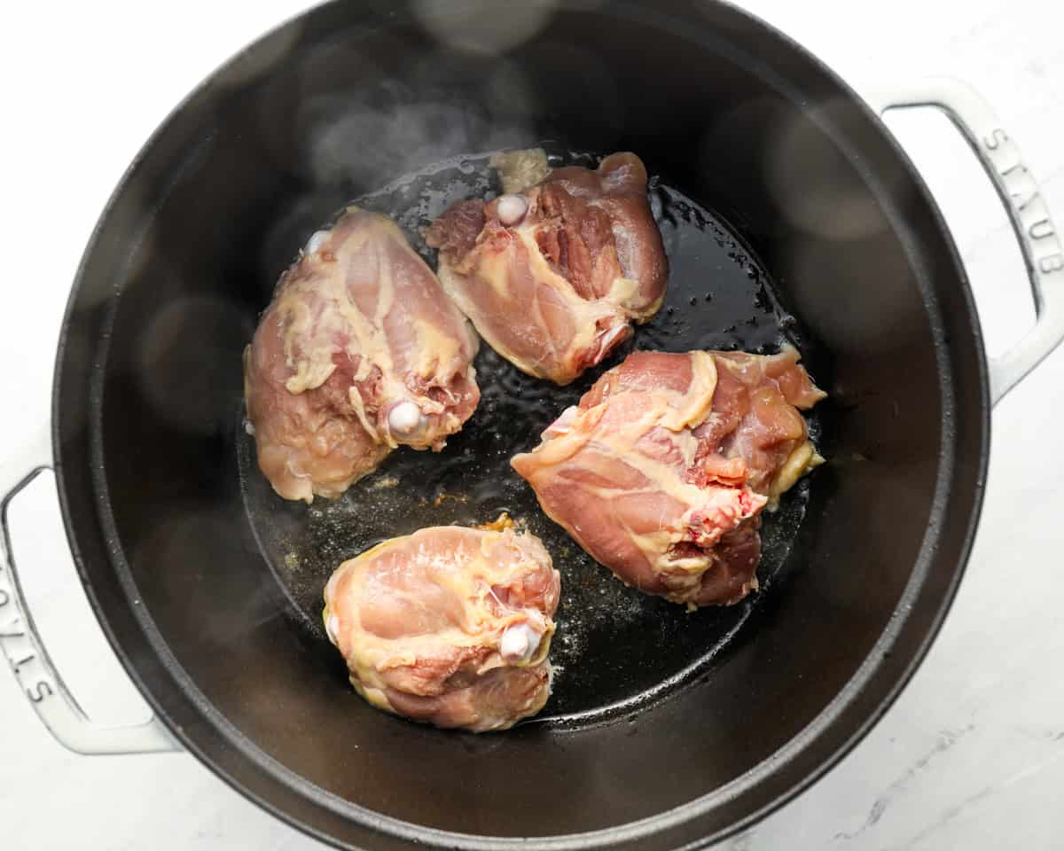 Raw chicken thighs sizzling in a black pot as the initial step of preparing matzo ball soup.