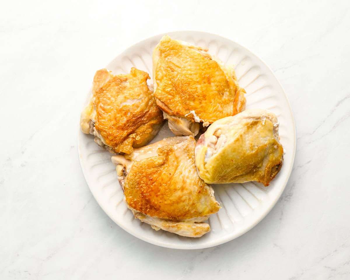 Golden-browned chicken thighs on a white plate after searing, ready to be added to the soup.