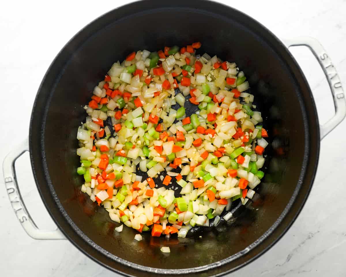 A pot with sautéed vegetables and a hint of garlic, beginning to soften as the base for matzo ball soup.