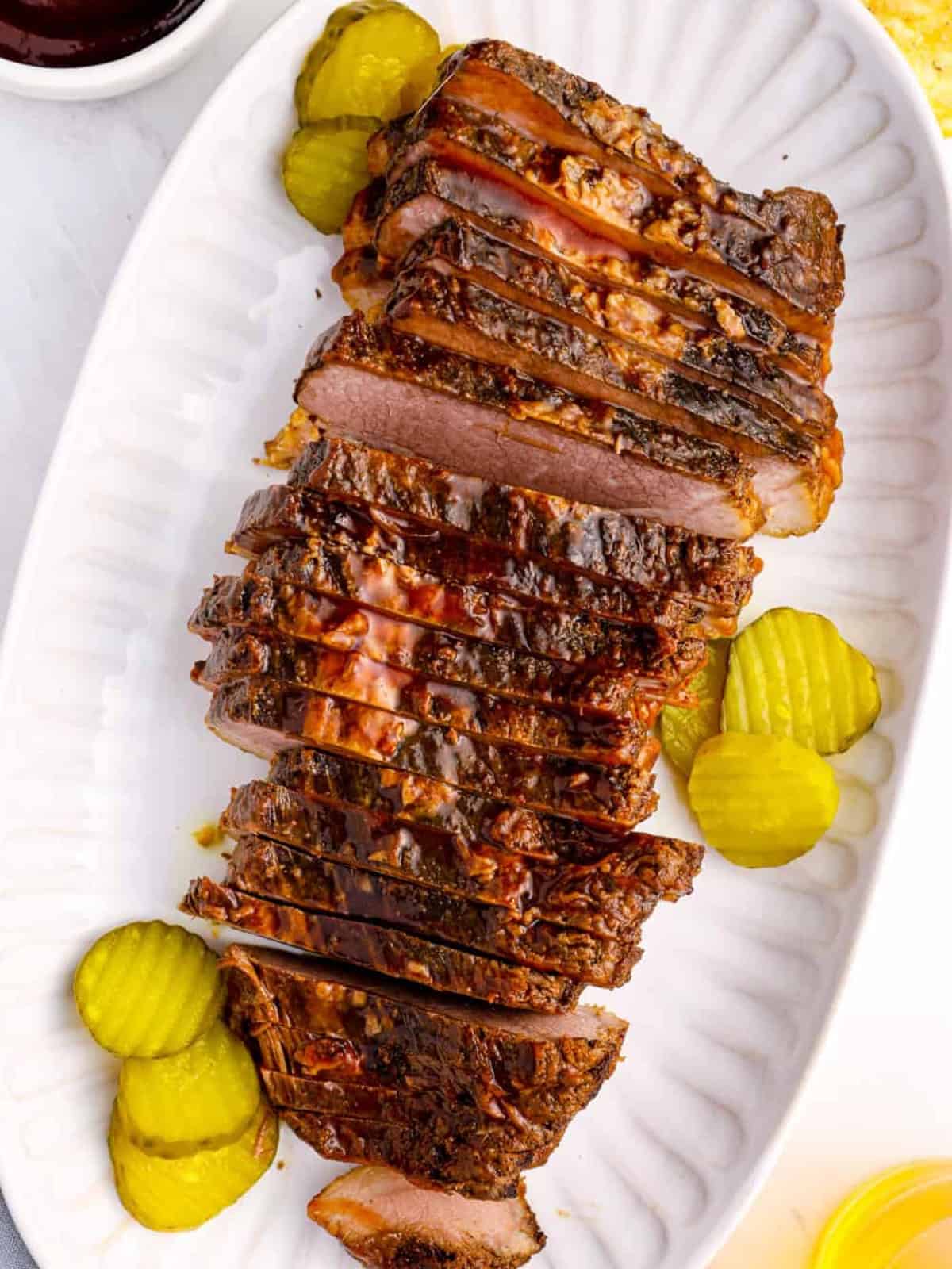 Overhead view of sliced brisket on a white platter with pickle slices.